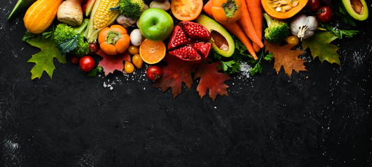 Autumn vegetables and fruits on a black stone background: Pumpkin, tomatoes, corn, pomegranate, persimmon, apple. Top view. Free copy space.