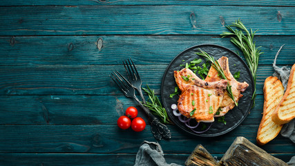 Pork steak on a bone with rosemary and greens in a black plate. Top view. Free copy space.
