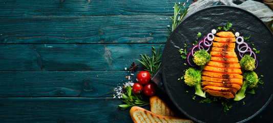 Baked pumpkin with vegetables on a black plate. Top view. Free copy space.
