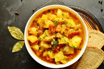 Vegetable stew in a white bowl on a dark wooden background. A dish of potatoes. Appetizing hot food, with vegetables. Vegetable Vegetarian Stew. Bowl with potatoes on a wooden board for serving dishes