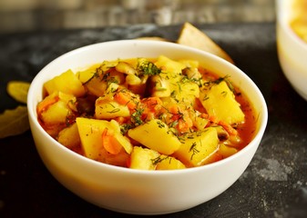 Vegetable stew in a white bowl on a dark wooden background. A dish of potatoes. Appetizing hot food, with vegetables. Vegetable Vegetarian Stew. Bowl with potatoes on a wooden board for serving dishes