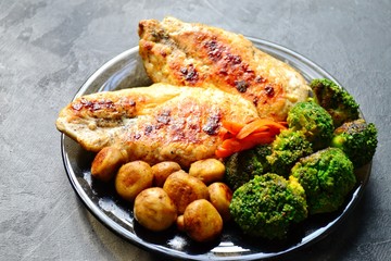 Grilled chicken breast. Appetizing grilled chicken fillet. Meat with vegetables, broccoli and mushrooms. Food on a dark background. Chicken on the plate and wooden board