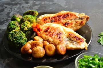 Grilled chicken breast. Appetizing grilled chicken fillet. Meat with vegetables, broccoli and mushrooms. Food on a dark background. Chicken on the plate and wooden board