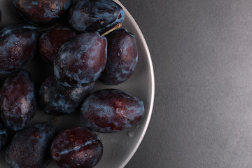 Fresh appetizing plums in a gray bowl, summer concept, copy space.