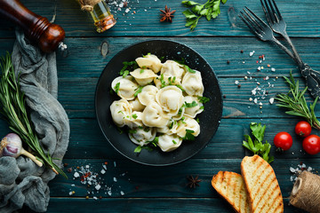 Russian pelmeni meat Dumplings with greens in a black plate. Russian traditional cuisine. Top view....