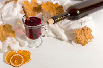 A cup of mulled wine with spices, bottle, a scarf, dry leaves and oranges on the table. Autumn...