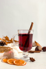A cup of mulled wine with spices, scarf, spices, dry leaves and oranges on the table. Autumn mood, a method to keep warm in the cold, copy space.