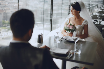 The stylish and elegant bridegroom and his pretty wife sitting in a restaurant