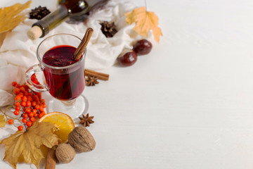A cup of mulled wine with spices, bottle, scarf, spices, dry leaves and oranges on the table. Autumn mood, method to keep warm in cold, copy space.