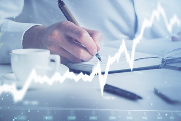 Double exposure of man's hands writing notes of stock market with forex chart.