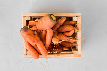 Ugly carrots in a wooden box on a gray concrete background. Top view, close-up, copy space.Vegetarian and healthy food. The concept of using fertilizers and GMOs.
