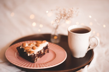 Chocolate pastry with hot black tea on wooden tray in bed. Good morning.
