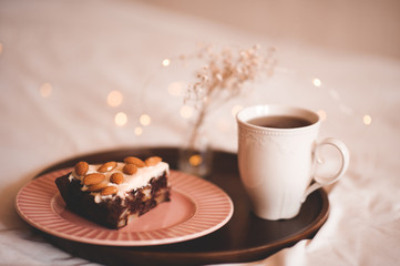 Chocolate unbaked pastry with almond nuts and cup of tea in bed over lights at background. Good morning. Winter season concept.