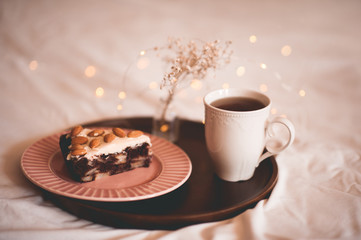 Chocolate cake with almond cuts and cup of tea on wooden tray in bed closeup. Breakfast time. Good morning.