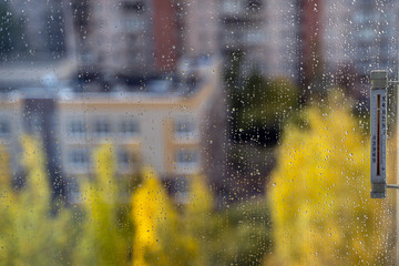 Rains drops on window. Blured. Street thermometer measures the weather outside the window. view from the window on the autumn yard