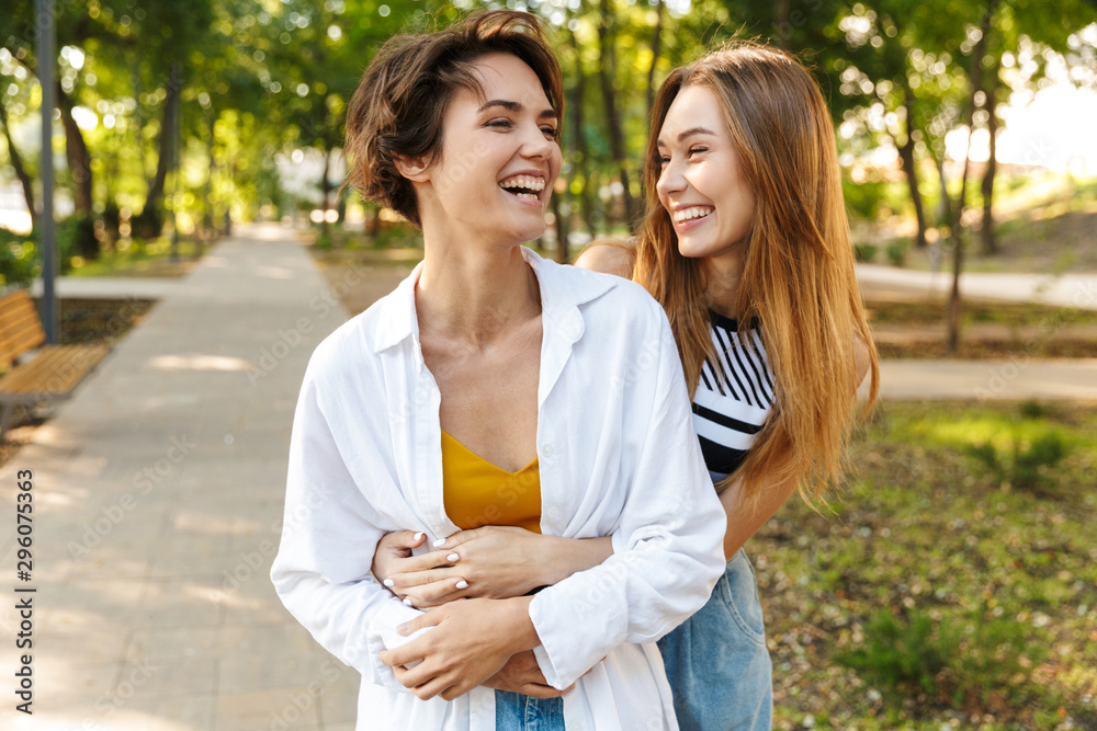 Poster Photo of two women hugging and laughing while walking in green park