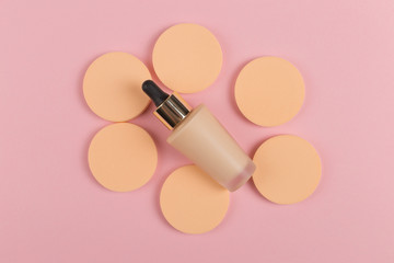 Sponges, a beautiful blender for applying foundation or powder and a bottle of concealer. Flat lay on a pink background, copy space.