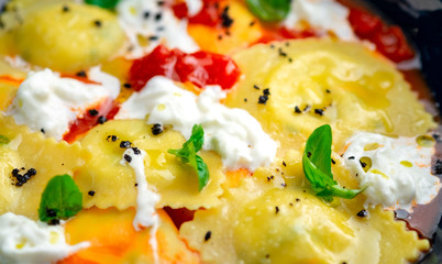Colorful cooked ravioli with tomato, Basil and cream cheese in a plate on a wooden background. Italian pasta rustic style