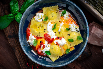 Colorful cooked ravioli with tomato, Basil and cream cheese in a plate on a wooden background. Italian pasta rustic style
