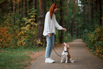 young ginger woman taming her pet perform some commands. full length side view photo.