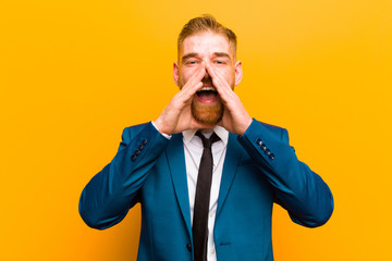 young red head businessman feeling happy, excited and positive, giving a big shout out with hands next to mouth, calling out against orange background