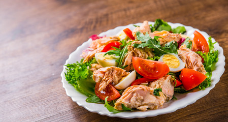 Fresh salad with fish, arugula, eggs,red pepper, lettuce, fresh sald leaves and tomato on a white plate on wooden table background