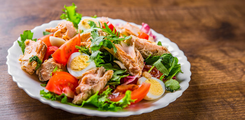 Fresh salad with fish, arugula, eggs,red pepper, lettuce, fresh sald leaves and tomato on a white plate on wooden table background