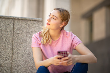 teen girl with blond hair holding mobile phone and looking away