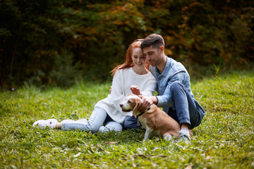 Fototapeta premium Happy loving couple relaxing on grass stroking dog, full length photo. family, friendship