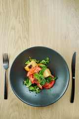 salad with fried halumi cheese cherry tomatoes and microgreen in black bowl on wooden background. Restaurant food