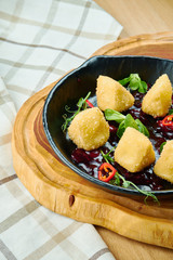Deep fried crispy Camembert with cranberry sauce in a decorative pan on wooden background. Close up, selecive focus