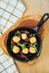 Deep fried crispy Camembert with cranberry sauce in a decorative pan on wooden background. Close up, selecive focus