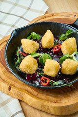 Deep fried crispy Camembert with cranberry sauce in a decorative pan on wooden background. Close up, selecive focus