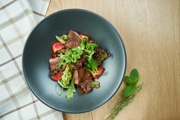 Grilled veal salad with lettuce, cherry tomatoes, dor blue cheese in a black bowl on wooden background. Selective focus, close up