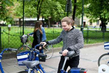 Young boy standing with hired bike near park with green trees.