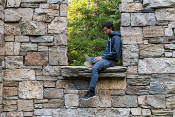 Young man working on laptop outdoors framed in window of abandoned building