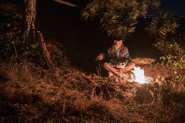caucasian male hunter resting in forest. near campfire with his dog, shotgun, ammunition, backpack on the background