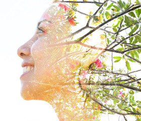Double exposure close up profile portrait of a young pretty woman interwoven with tree branches and delicate colorful flowers seemingly growing from her hair