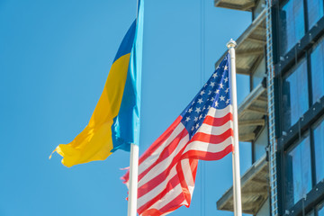 American and Ukrainian flags fly against the blue sky and part of the building. Patriotism.