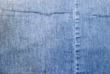 Texture of a blue denim fabric with yellow stains. Two pieces of fabric stitched together