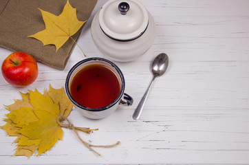 tea in a white cup with white sugar in cubes and cane sugar, maple leaves and apples on a wooden light background.