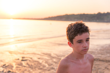 le portrait d'un jeune garçon sur la plage avec un coucher de soleil romantique