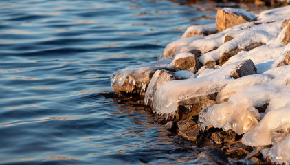 Icy bank and cold open water in the coast of Yakutia, Sakha Republic at sunset. Relaxing view of a stones in the water with an ice cap at sunset.