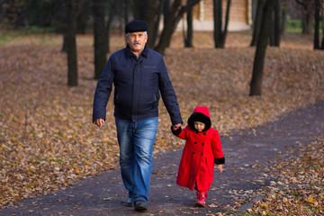 Fototapeta premium Mature man and little girl holding hands walkking in autumn park