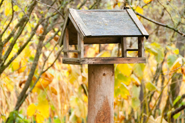 Wooden homemade small log bird feeder house with large windows for feeding birds on a tree close up