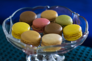 Macarons of different colors on glass stand for sweets on blue textile background