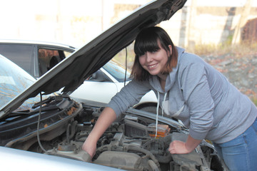 Fototapeta na wymiar Beautiful young woman, brunette, repairs a car, looks under the hood