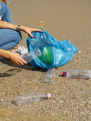 Young woman collecting recyclable plastic bottles on the beach
