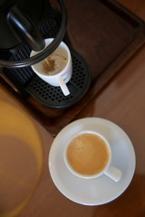 Two cups of freshly prepared coffee and a coffee maker on the wooden table