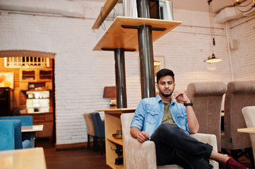 Portrait of handsome successful bearded south asian, young indian freelancer in blue jeans shirt sitting in cafe and having a rest.